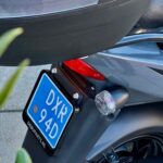 Achterkant van een grijze scooter met blauw kenteken, achterlicht en knipperlicht.