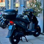 Zwarte Kymco Agility scooter met topkoffer, op middenbok geparkeerd bij showroom.