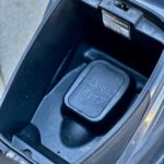 Open opbergruimte onder het zadel van een scooter met CARB. MAINT-klep en label.