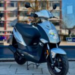 Zilveren Kymco-scooter op de standaard voor een winkelraam in de stad, close-up van de voorkant.