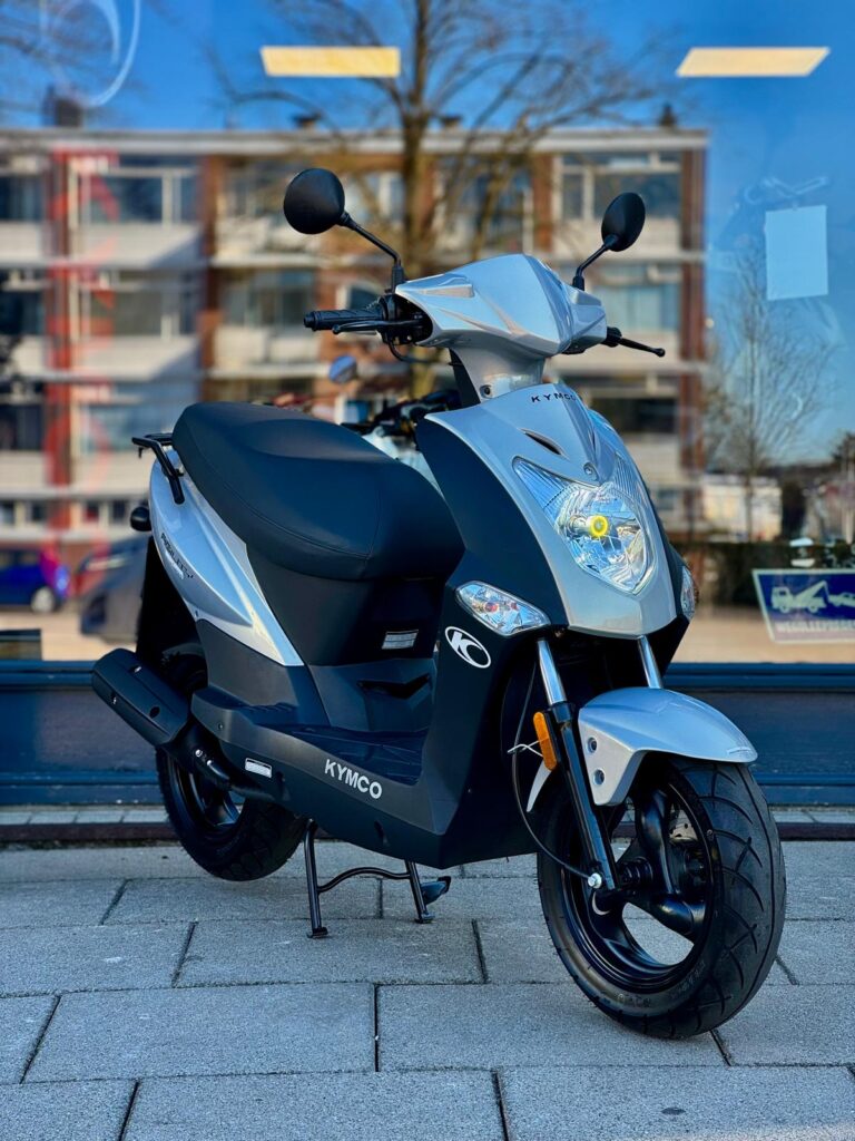 Zilveren Kymco-scooter op de standaard voor een winkelraam in de stad, close-up van de voorkant.