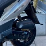 Close-up van de achterzijde van een grijze Kymco Agility scooter met wiel en veer.