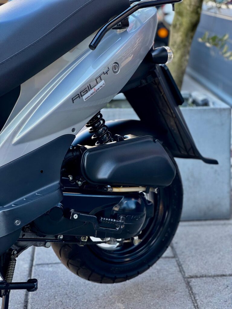 Close-up van de achterzijde van een grijze Kymco Agility scooter met wiel en veer.