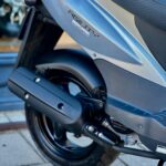 Close-up van de achterzijde van een Kymco Agility scooter met uitlaat en achterwiel.