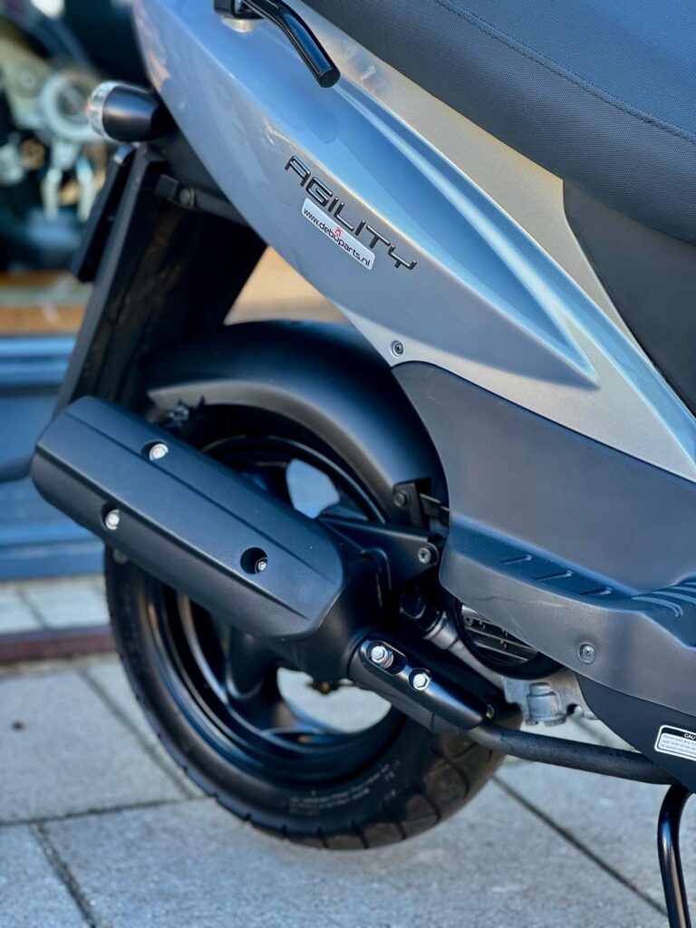 Close-up van de achterzijde van een Kymco Agility scooter met uitlaat en achterwiel.