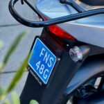 Achterkant van een grijze scooter met blauw kenteken, bagagedrager en achterlicht.