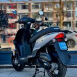 Zwarte en zilveren Kymco Agility scooter op standaard, geparkeerd op stoep voor een etalage.