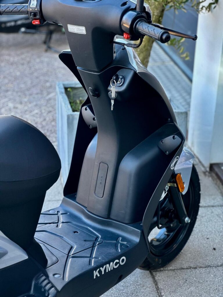 Close-up van een zwarte Kymco-scooter met sleutel in het contact, geparkeerd buiten.