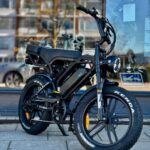 Zwarte fatbike met dikke Kenda-banden en koplamp, geparkeerd voor een winkelraam.