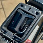 Close-up van de accuhouder met laadkabel onder het zadel van een elektrische scooter.