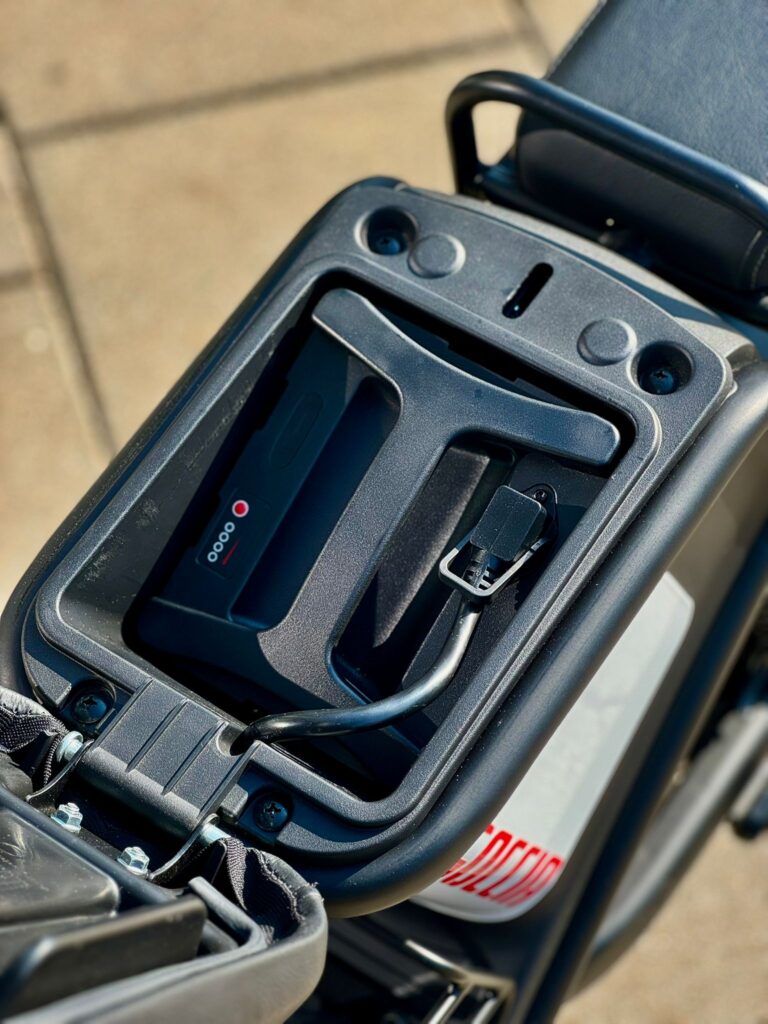 Close-up van de accuhouder met laadkabel onder het zadel van een elektrische scooter.