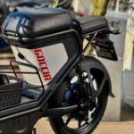 Close-up van de achterzijde van een zwarte Goccia e-scooter met zadel, veer en bagagedrager.