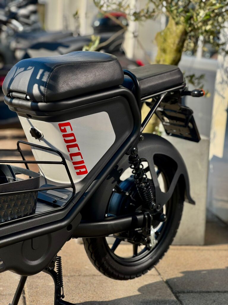 Close-up van de achterzijde van een zwarte Goccia e-scooter met zadel, veer en bagagedrager.