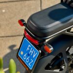 Close-up van het achterdeel van een zwarte scooter met blauw NL-kenteken en oranje richtingaanwijzers.