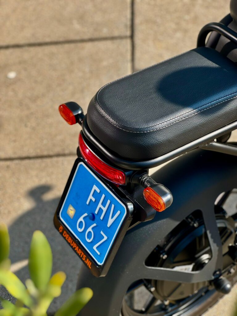 Close-up van het achterdeel van een zwarte scooter met blauw NL-kenteken en oranje richtingaanwijzers.