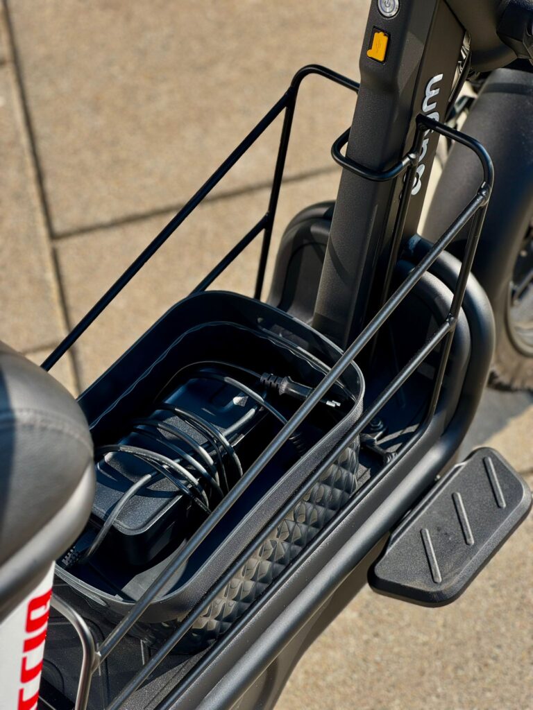 Close-up van e-bike met opbergvak met lader en kabel, naast voetsteun.