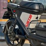 Close-up van een zwarte elektrische Goccia-scooter met bagagedrager, achterwiel en vering buiten geparkeerd