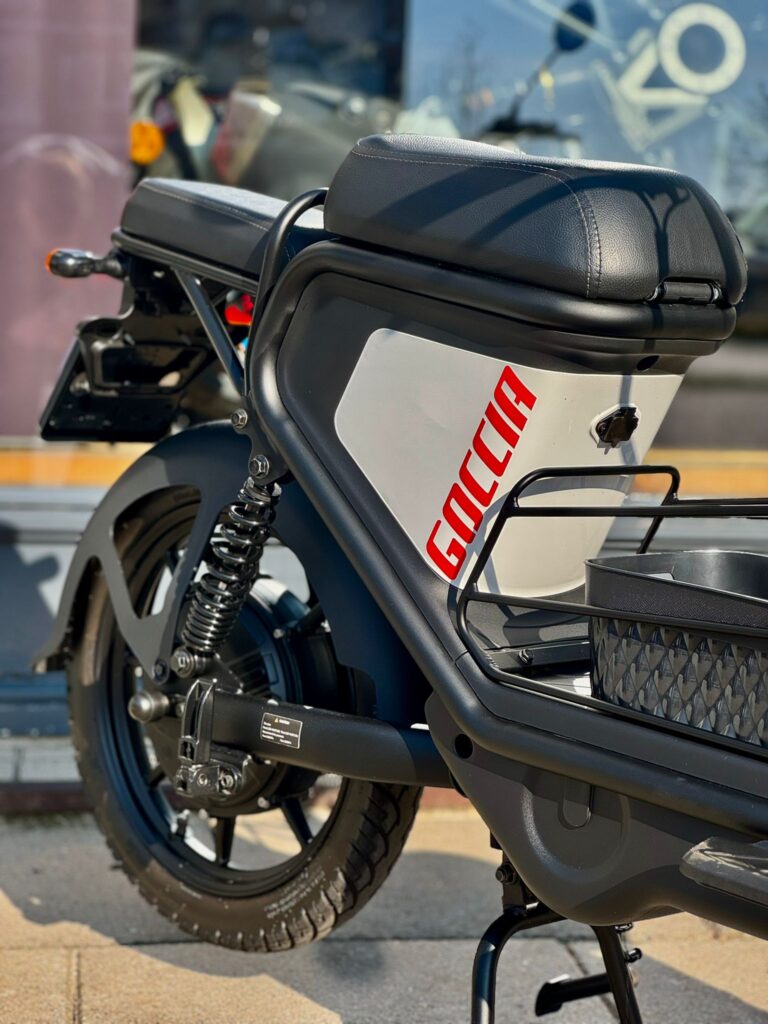 Close-up van een zwarte elektrische Goccia-scooter met bagagedrager, achterwiel en vering buiten geparkeerd