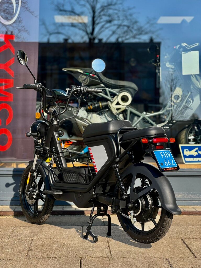 Zwarte elektrische bromfiets met blauw NL-kenteken, geparkeerd voor een winkelruit.