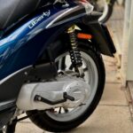 Close-up van het achterwiel, veer en motorblok van een blauwe Liberty-scooter.