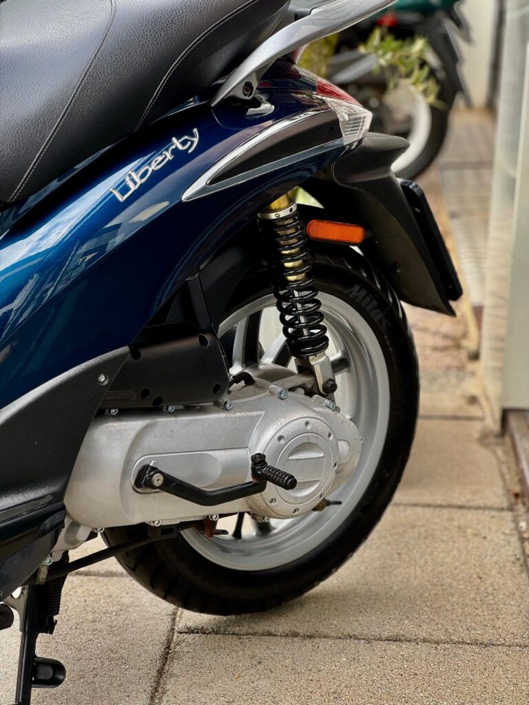 Close-up van het achterwiel, veer en motorblok van een blauwe Liberty-scooter.