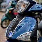 Close-up van een blauwe scooter met koplamp en richtingaanwijzers, met onscherpe scooters op de achtergrond.