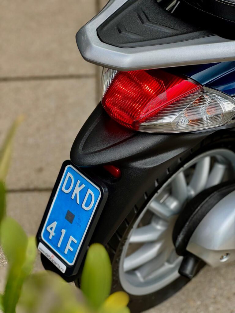 Close-up van het achterlicht, wiel en blauwe kentekenplaat van een scooter.