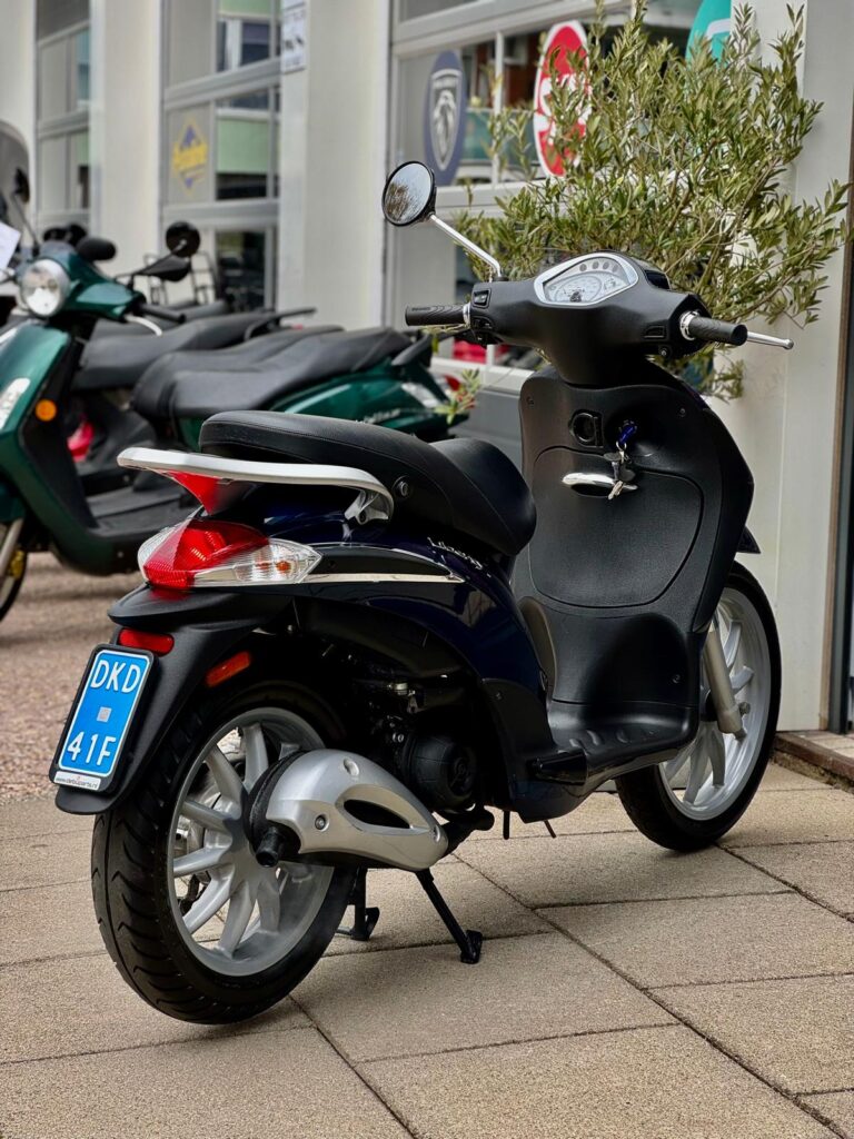 Zwart-blauwe scooter op zijstandaard met blauw kenteken, geparkeerd voor een showroom met scooters.