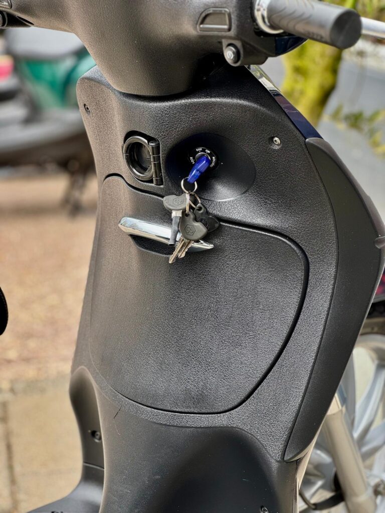 Close-up van een scooter met sleutels in het contactslot bij het stuur.