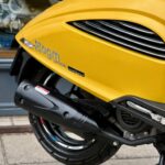 Close-up van de rechterachterzijde van een gele AGM-scooter met uitlaat en achterwiel.