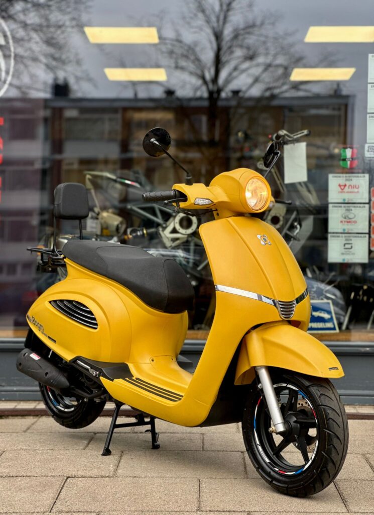Gele scooter met zwart zadel, op standaard geparkeerd voor een winkelruit