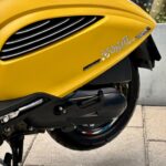 Close-up van de gele zijkant van een AGM Supreme scooter met luchtroosters en achterwiel op de stoep.