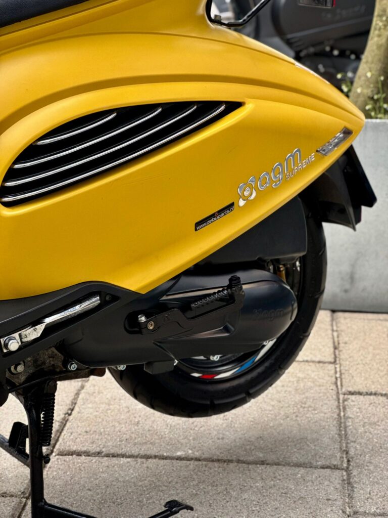 Close-up van de gele zijkant van een AGM Supreme scooter met luchtroosters en achterwiel op de stoep.