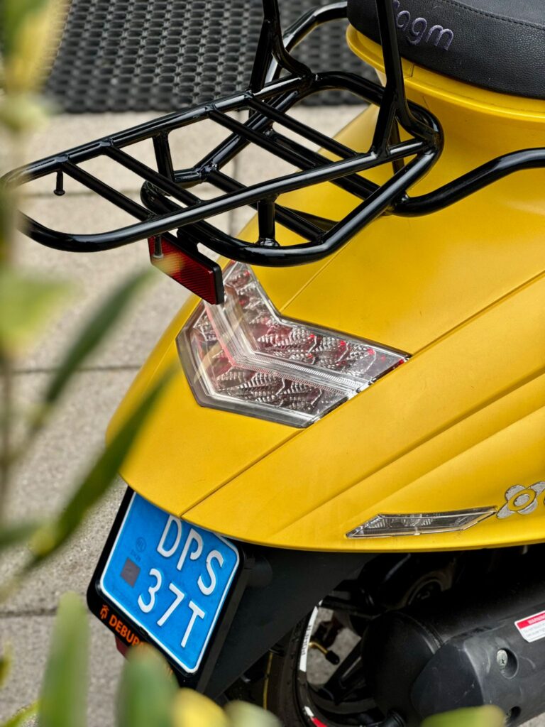 Gele scooter van achteren met bagagedrager, achterlicht en blauwe kentekenplaat