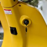 Close-up van het contactslot van een gele scooter met een ingestoken sleutel.
