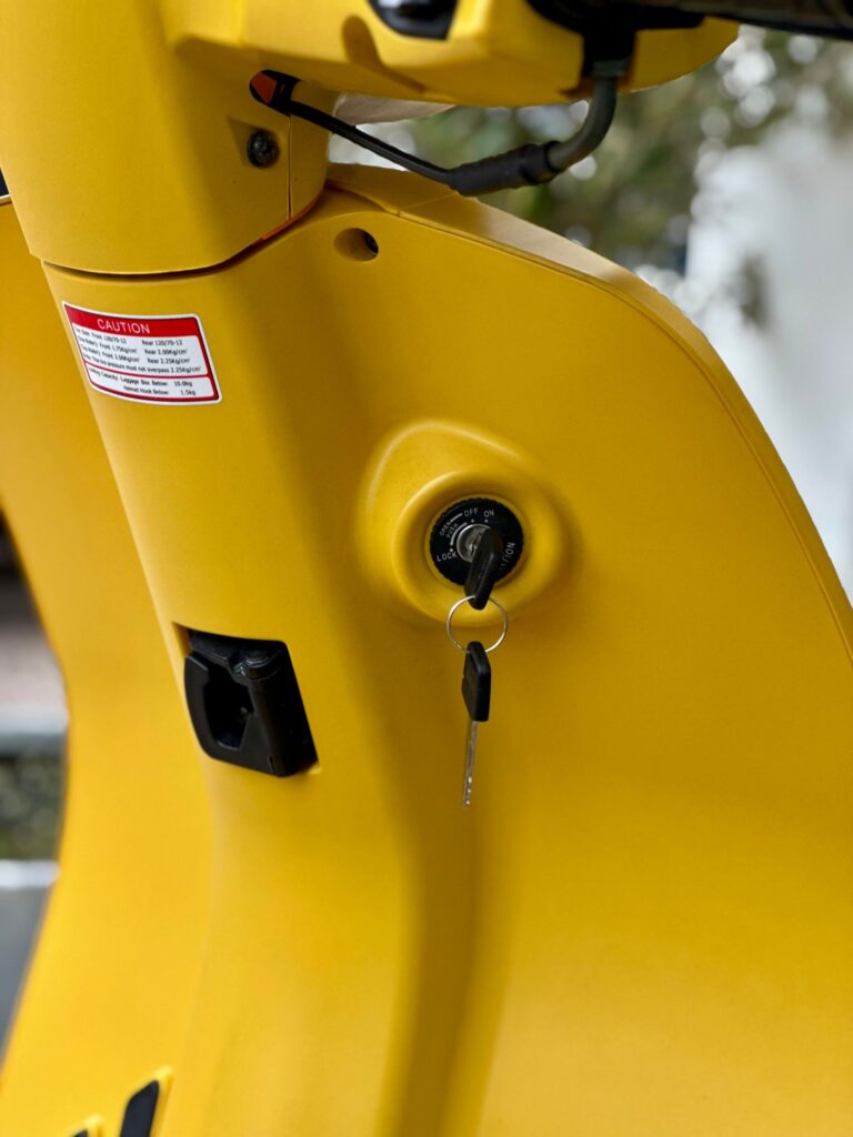 Close-up van het contactslot van een gele scooter met een ingestoken sleutel.