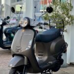 Matgrijze Sourini-scooter met windscherm en bagagedrager voor een showroom.