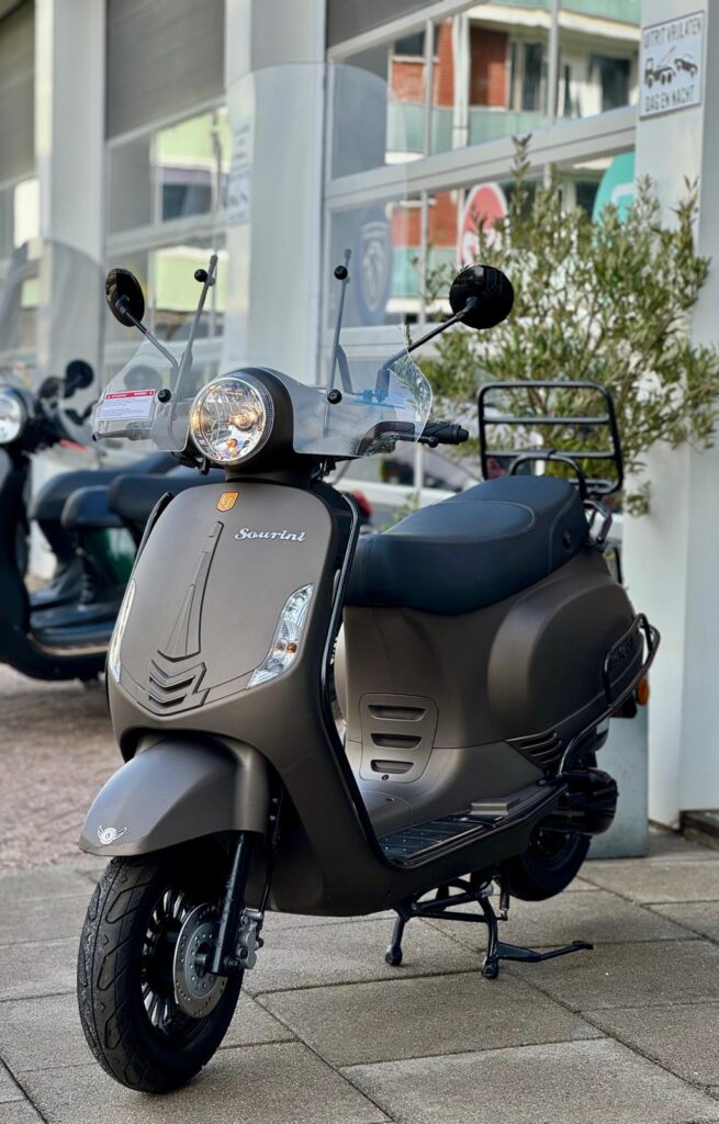 Matgrijze Sourini-scooter met windscherm en bagagedrager voor een showroom.