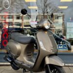 Matbrons retro-scooter met hoog windscherm geparkeerd voor een winkelraam in de stad.