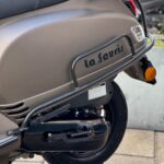 Close-up van de achterzijde van een matte La Souris-scooter met bagagerek, uitlaat en achterlicht.