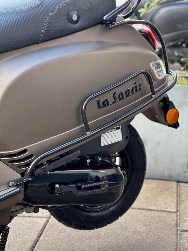 Close-up van de achterzijde van een matte La Souris-scooter met bagagerek, uitlaat en achterlicht.