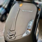 Close-up van de voorkant van een matte bronskleurige scooter met Sourini-logo en richtingaanwijzers.