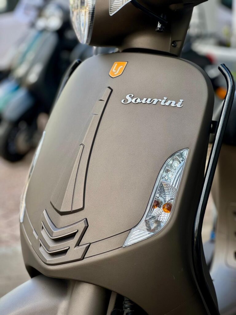 Close-up van de voorkant van een matte bronskleurige scooter met Sourini-logo en richtingaanwijzers.