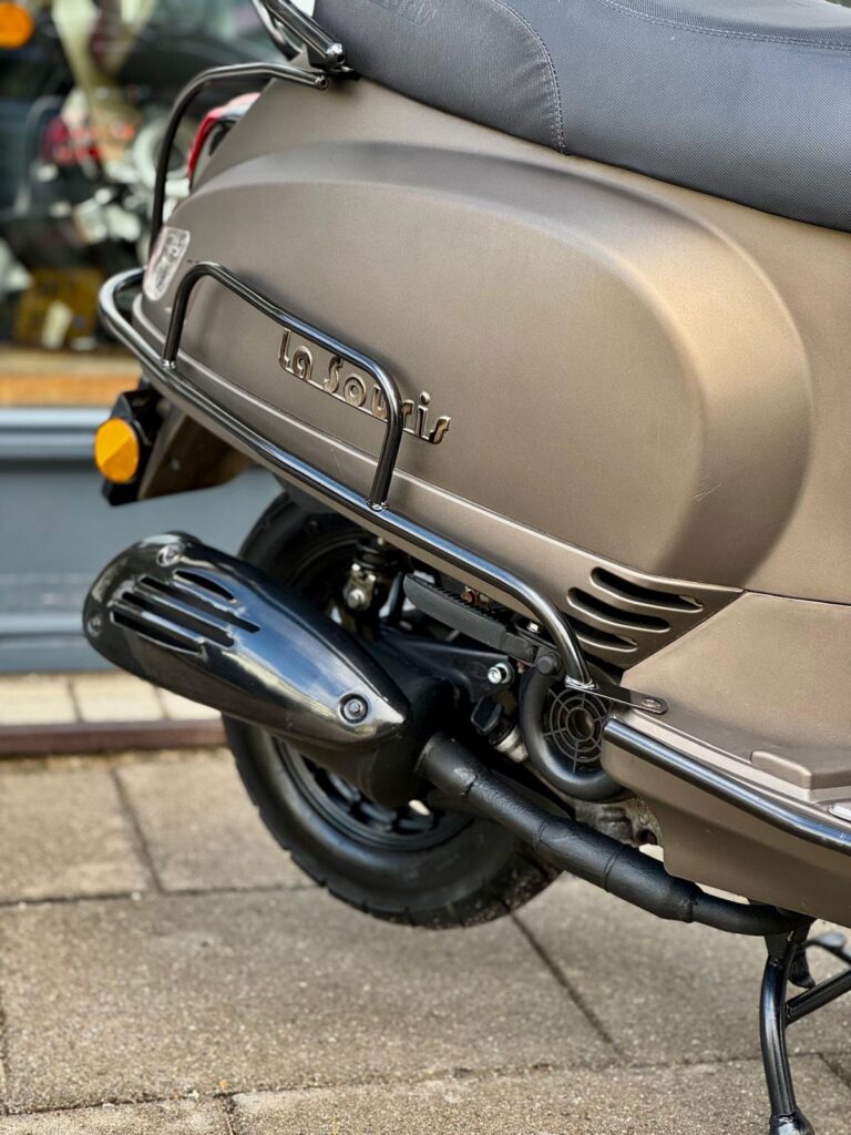 Close-up van de achterkant van een matte bronzen La Souris scooter met uitlaat en bagagerek.