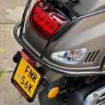 Achterzijde van een scooter met rood achterlicht, geel NL-kenteken en zwarte bagagedrager.