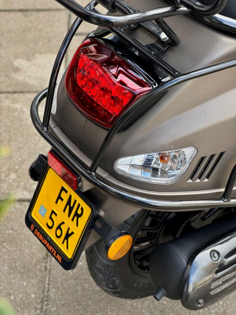 Achterzijde van een scooter met rood achterlicht, geel NL-kenteken en zwarte bagagedrager.