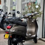 Matgrijze La Souris retro-scooter met bagagerek, op de standaard voor een scootershop.