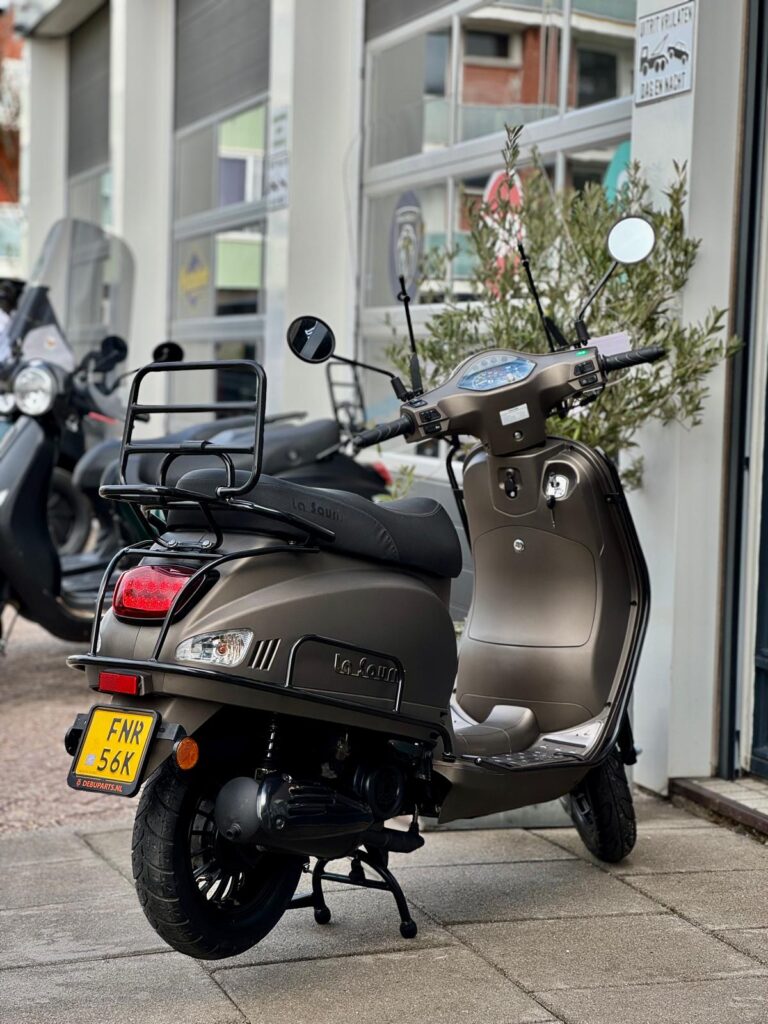 Matgrijze La Souris retro-scooter met bagagerek, op de standaard voor een scootershop.