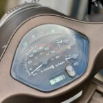 Close-up van het dashboard van een scooter met snelheidsmeter, brandstofmeter en digitaal klokje 9:38.