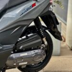 Close-up van de achterzijde van een grijze SYM Orbit III scooter met veer en motorblok.